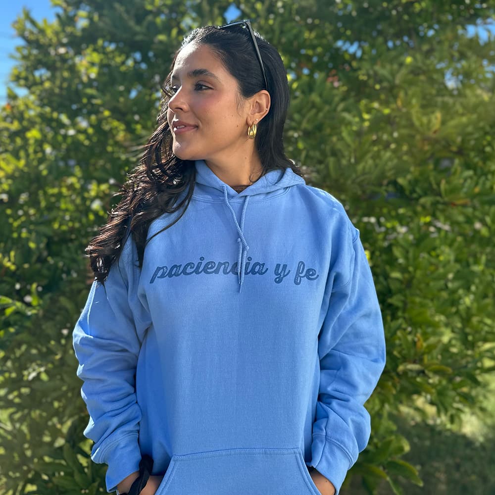 Heather gray drawstring hoodie with navy cursive "paciencia y fe" text, Broadway-inspired fan merch.