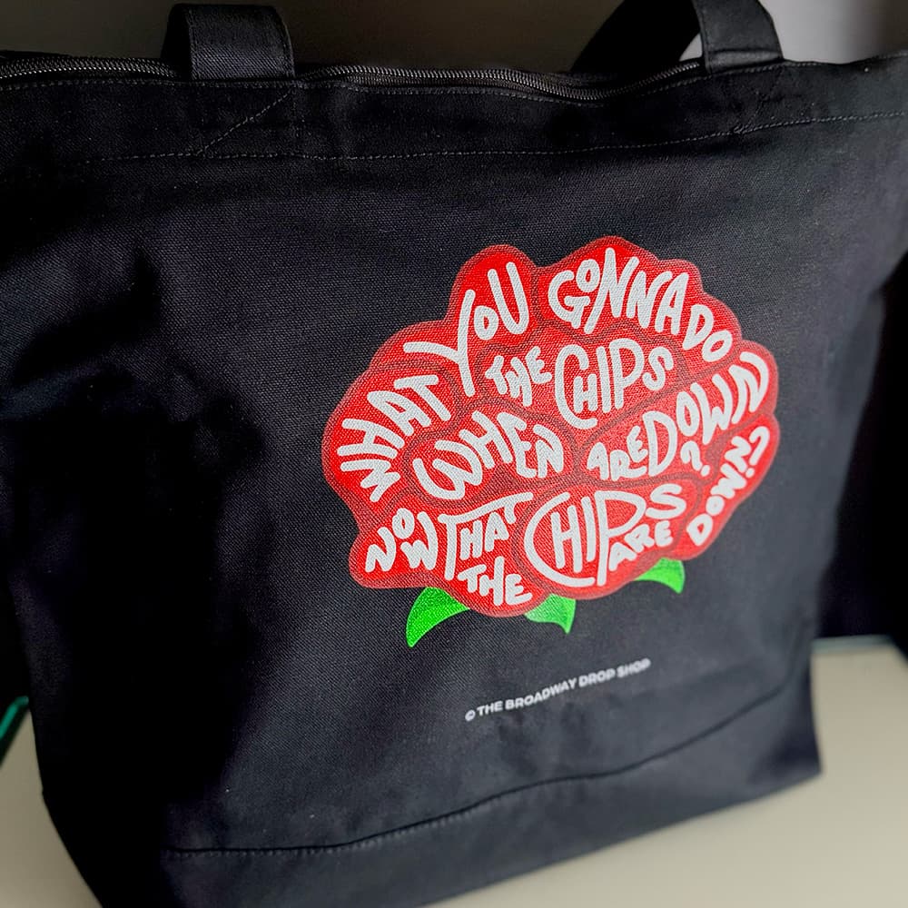 Black canvas zip tote bag with red rose design and playful hand-lettered "chips are down" text.